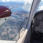 Cockpit view from a Cessna 414, looking out the left window at sunny skies and clouds over terrain 6,500 feet below